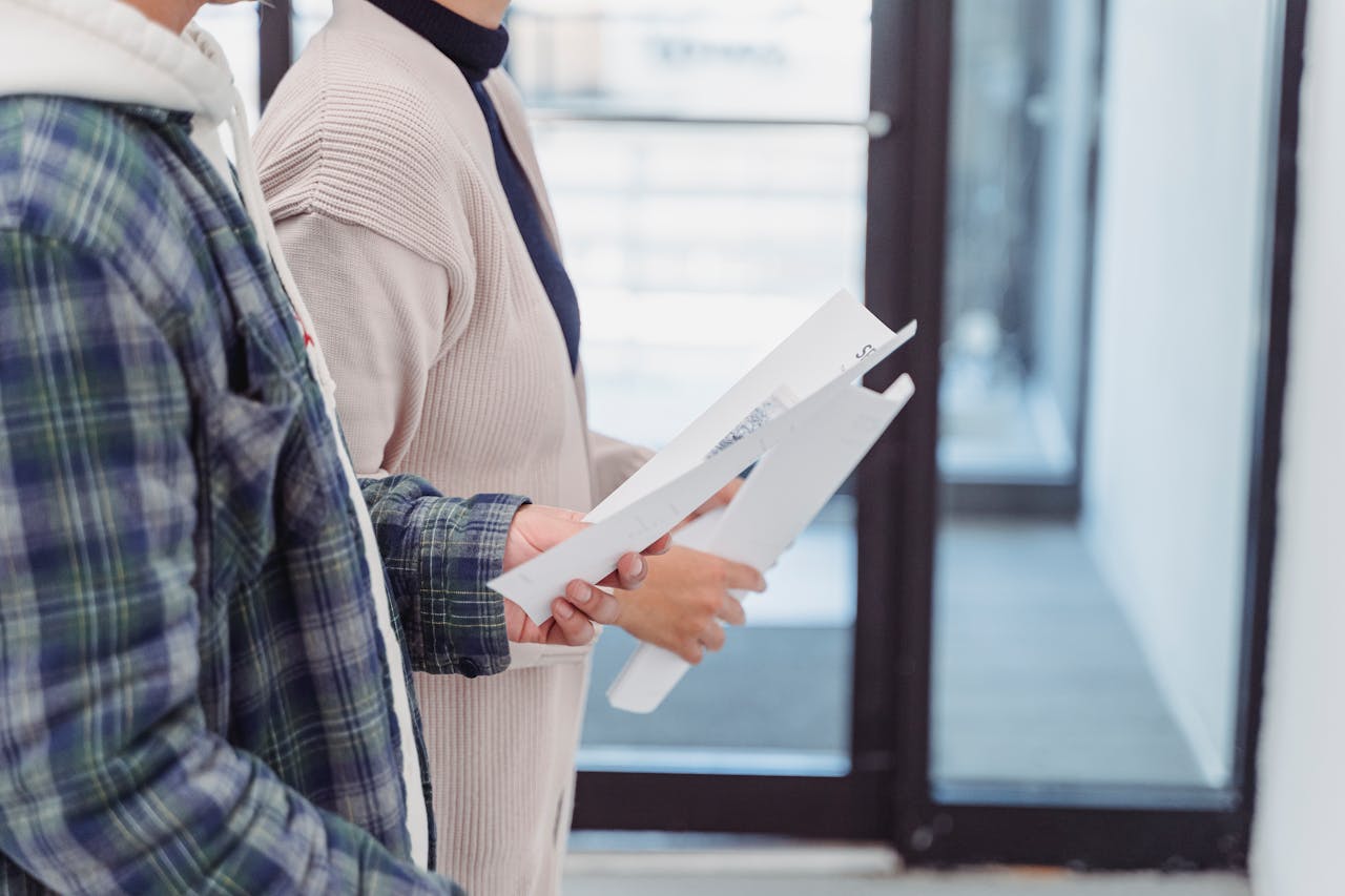 Two individuals standing indoors holding documents, possibly discussing work matters.